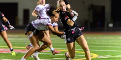 Ayala Bulldogs flag football player runs with the ball while breaking a tackle from a Claremont Wolfpack defender during a night game.
