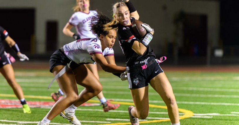 Ayala Bulldogs flag football player runs with the ball while breaking a tackle from a Claremont Wolfpack defender during a night game.